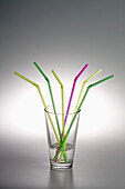 A glass with water in it and three yellow drinking straws, two green ones and one pink one