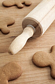 Unfrosted gingerbread men on a wood table with a rolling pin, close-up