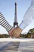 A man and woman holding hands in front of the Eiffel Tower, focus on hands