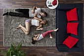 A family of three happily lying on a living room rug, overhead view