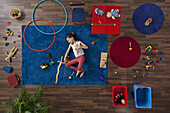 A little girl lying on a rug with toys, overhead view