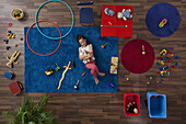 A little girl lying on a rug hugging stuffed animals, overhead view