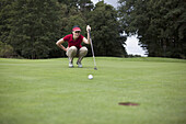 A female golfer crouching down studying the distance to the hole