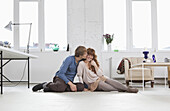 A young man kissing his girlfriend, side by side, sitting on floor