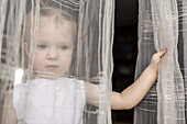 Girl looking out between curtains of open window