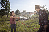 Girl sprays guy with hose in a field