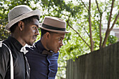 Two young black men dressed in bow ties and hats, looking away