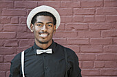 A cheerful young black man wearing bow tie, suspenders and hat