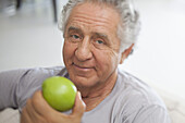 A senior man preparing to eat a green apple