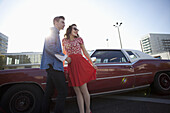 A cheerful rockabilly couple standing next to a vintage car