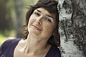 A serene woman leaning against a tree trunk