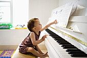A little boy sitting at a piano reaching out with curiosity for the sheet music