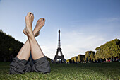A woman laying in grass by Eiffel Tower, focus on feet