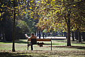 A shirtless businessman reading a newspaper on a park bench