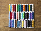 Rows of various colored spools of thread on a wooden table