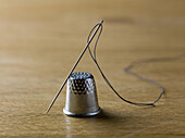 A threaded needle balanced against a shiny metal thimble