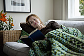 A woman reading a book while reclining on a sofa