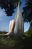 A woman sitting in a closed up hammock hanging from a tree, only legs visible