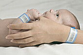 A baby holding her mother's thumb, both wearing hospital ID bracelets