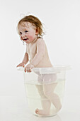 A baby girl standing in a bucket of water