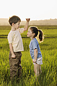 A boy and a girl in a field comparing heights