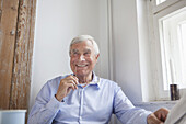 Thoughtful senior man smiling while holding glasses at home