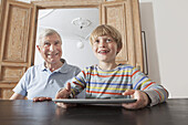 Happy senior man sitting by grandson with digital tablet at home