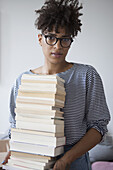 Portrait of confident young woman carrying stack of books at home