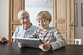 Senior man looking at grandson using digital tablet in house