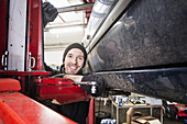 Portrait of confident male auto mechanic leaning on hoist in repair shop