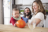 Happy parents looking at baby girl playing with pumpkin in kitchen
