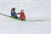 Full length of siblings tobogganing together in snow