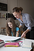 Mother helping daughter in doing homework at table