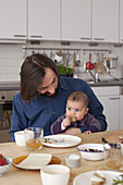 Family looking at baby girl eating bread at home