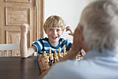 Happy grandson playing chess with grandfather at home