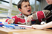 A small boy bothers his friend as he does his school work