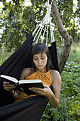 Young woman lying in hammock and reading