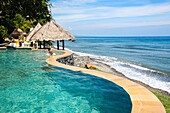 Woman in an infinity pool of a hotel with view to Indian Ocean, Amed, Bali, Indonesia