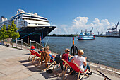 Young women sitting on deck chairs at Chicagokai, cruise liner Mein Schiff 1 and paddle steamer Louisiana Star in the background, Hamburg Cruise Center, Hamburg, Germany