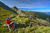 Frau beim Wandern blickt auf Landkarte, Berge im Hintergrund, Trans-Lagorai, Lagorai-Höhenweg, Lagorai, Dolomiten, UNESCO Welterbe Dolomiten, Trentino, Italien