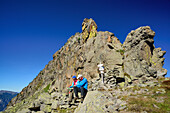 Zwei Wanderer sitzen unter Felsturm und blicken auf Karte, Trans-Lagorai, Lagorai-Höhenweg, Lagorai, Dolomiten, UNESCO Welterbe Dolomiten, Trentino, Italien