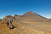 Zwei Wanderer auf der Tongariro Crossing, einem der Great Walks of New Zealand-Wanderpfade, in Höhe des Südlichen Kraters mit Blick auf den aktiven Vulkan Ngauruhoe, Tongariro National Park, Nordinsel, Neuseeland