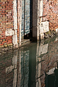Kanalspiegelung und Gemäuer mit Holztür, Venedig, Italien