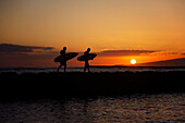 Hawaii, Oahu, Waikiki, Two Surfers Walking Along The Shoreline As The Beautiful Sunsets
