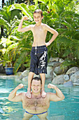 Boy Standing On His Father's Shoulders In Pool