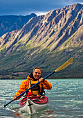 'Kayaker on Kusawa Lake with the setting sun hitting the mountains; Yukon, Canada'