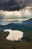 Aerial of dramatic clouds spilling light over the Philip Smith mountains in the Arctic National Wildlife Refuge, Brooks range mountains, Alaska.