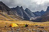 Backpackers enjoy a campsite on the autumn tundra with a view of East and West Maiden and Camel peaks in the distance, Arrigetch Peaks, Gates of the Arctic National Park, Alaska.