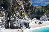 'People walking along a steep ridge at the coast with turquoise water and a waterfall; California, United States of America'