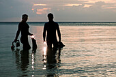 Indonesia, Silhouetted divers entering the ocean with lights at dusk